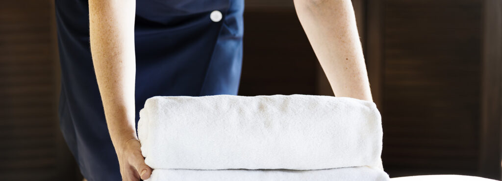 Housekeeping staff in a dark uniform carries a stack of clean white towels.