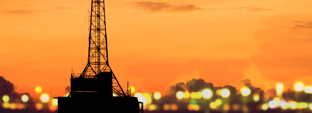 Silhouette of a tall communication tower on a rooftop against an orange sunset with blurred city lights in the background.